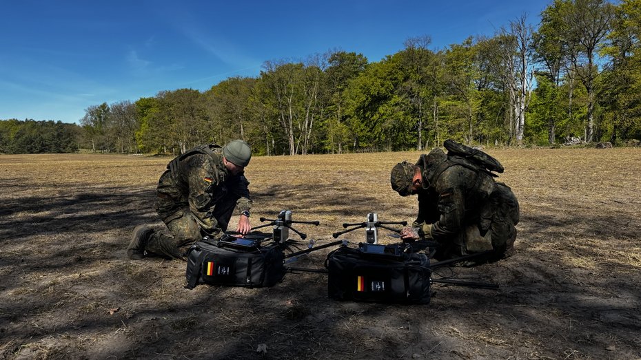 Two operators preparing AERIS Recon S7 UAV systems with mobile transport bags for field deployment in open terrain.